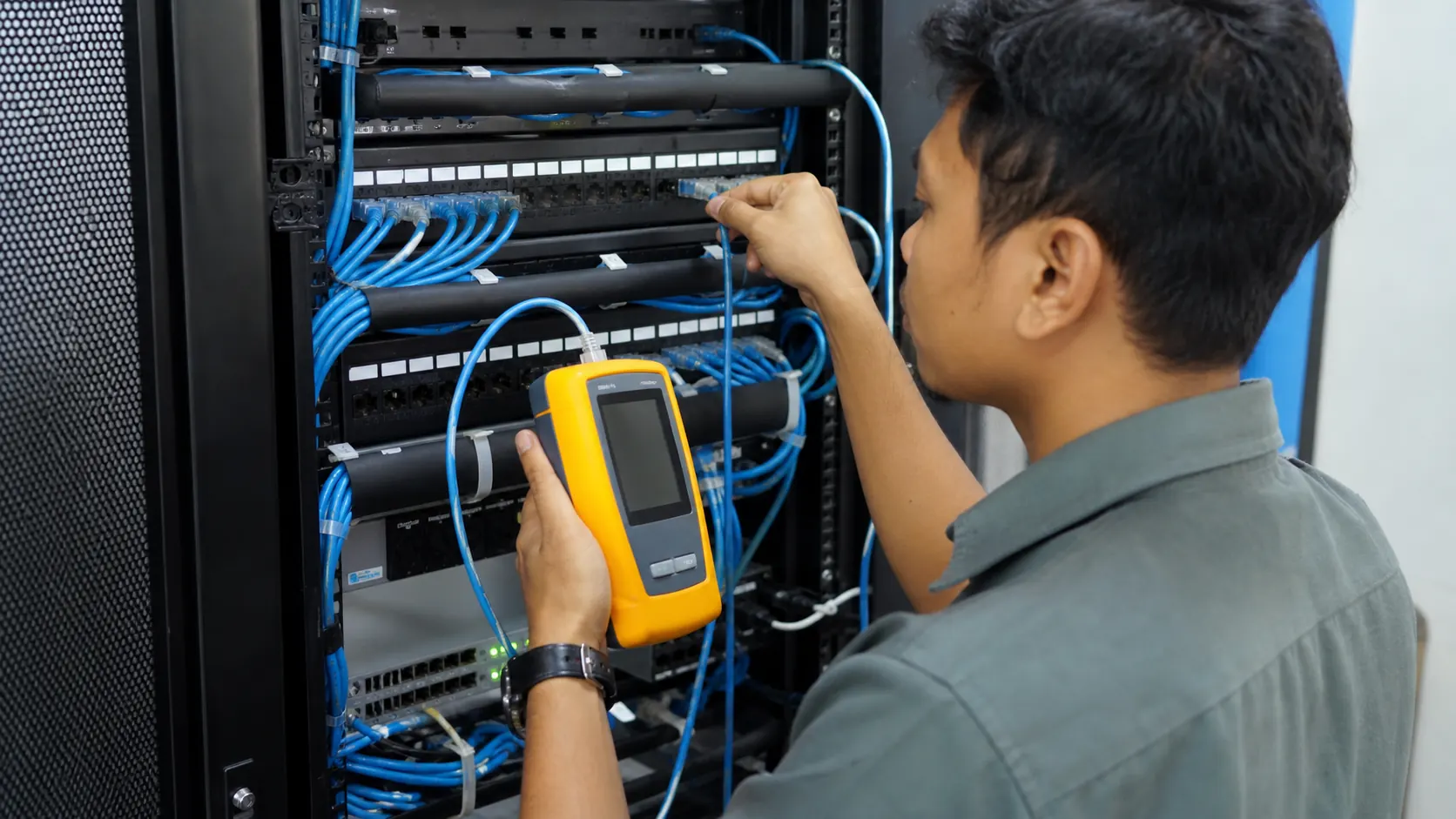 Teknisi menguji jalur kabel LAN pada patch panel menggunakan cable tester